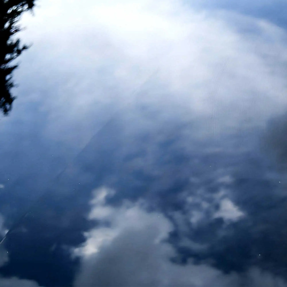 Car paint surface reflecting sky and clouds with smooth glossy finish after scratch removal