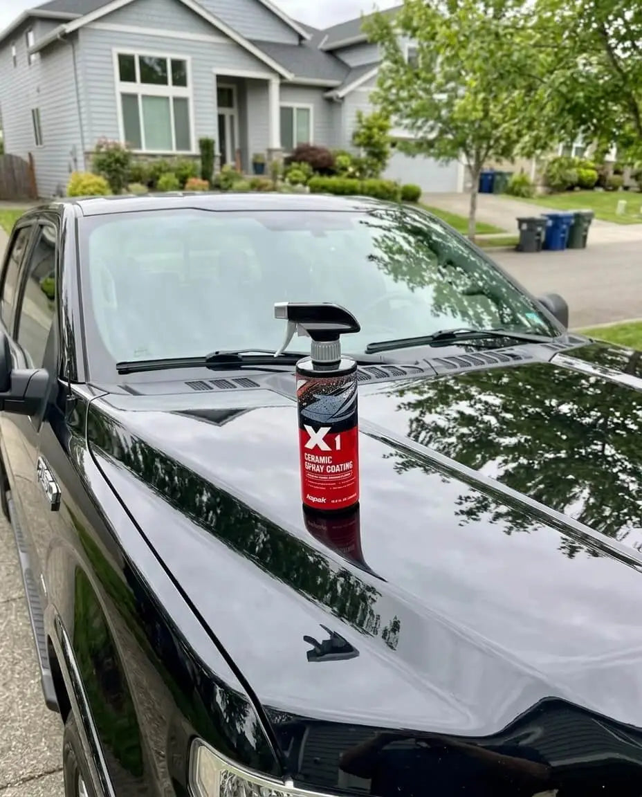 Kapak X1 ceramic spray coating bottle on black car hood with glossy reflective paint in residential driveway