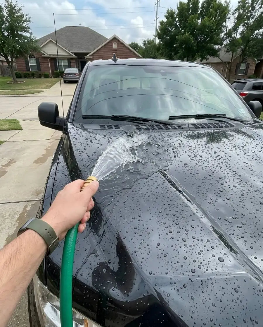 Water beading on black car hood after Kapak ceramic coating showing hydrophobic lotus effect during rinse