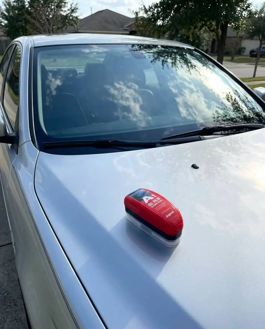 Kapak oil film cleaning brush placed on car hood with clean windshield reflecting sky and clouds