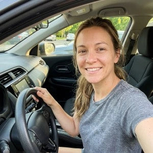 Woman smiling in driver seat holding steering wheel taking selfie inside car